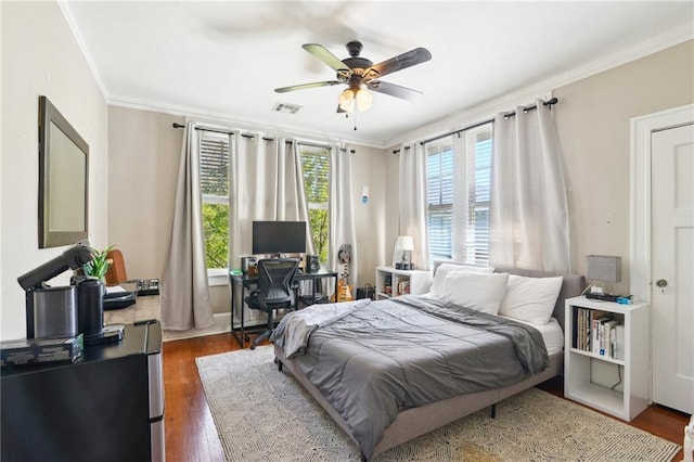 bedroom featuring ceiling fan, visible vents, wood finished floors, and ornamental molding