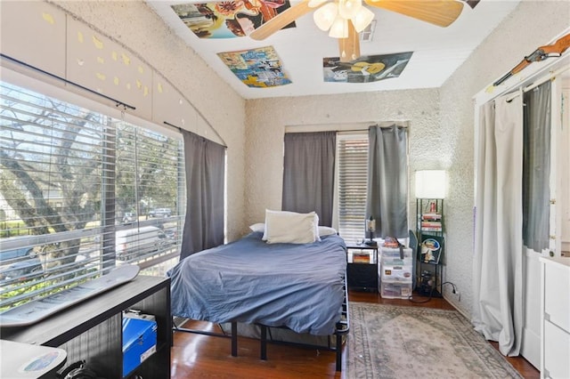 bedroom with a textured wall, visible vents, a ceiling fan, and wood finished floors