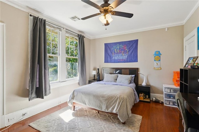 bedroom featuring visible vents, baseboards, ornamental molding, wood finished floors, and a ceiling fan