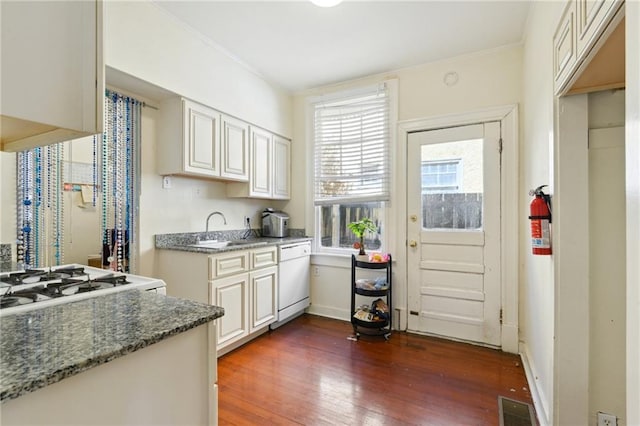 kitchen featuring wood finished floors, visible vents, dark stone counters, white dishwasher, and a sink