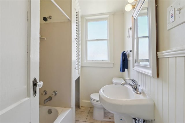 bathroom featuring toilet, wainscoting, shower / bathing tub combination, tile patterned floors, and a sink