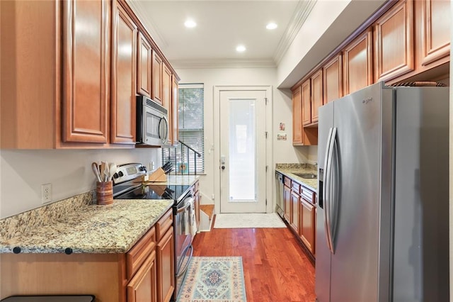 kitchen featuring wood finished floors, appliances with stainless steel finishes, brown cabinetry, crown molding, and light stone countertops