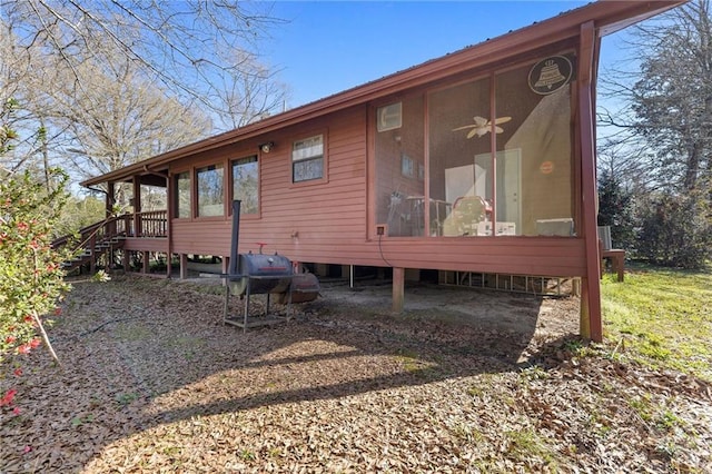 rear view of property with stairway, a sunroom, and ceiling fan