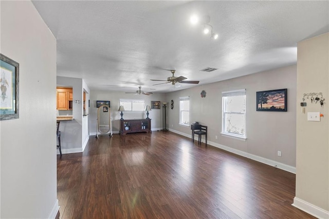 unfurnished living room featuring a ceiling fan, visible vents, dark wood-style floors, baseboards, and a textured ceiling