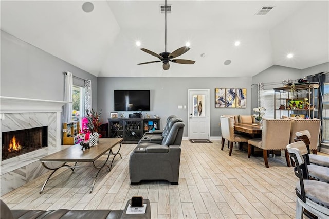 living area with light wood-type flooring, visible vents, lofted ceiling, and a high end fireplace