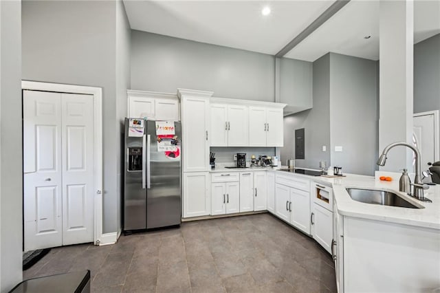 kitchen featuring light stone counters, a high ceiling, stainless steel fridge, white cabinetry, and a sink