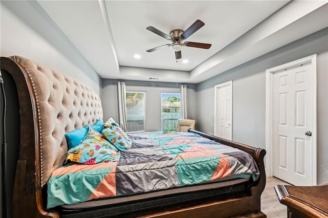 bedroom with recessed lighting, light wood-type flooring, a raised ceiling, and a ceiling fan