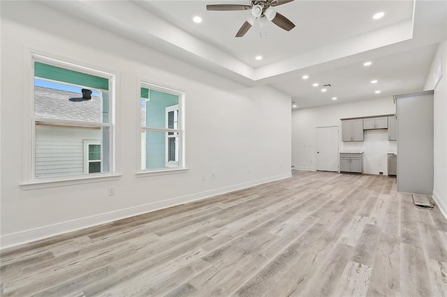 unfurnished living room with recessed lighting, baseboards, a raised ceiling, and light wood-style floors