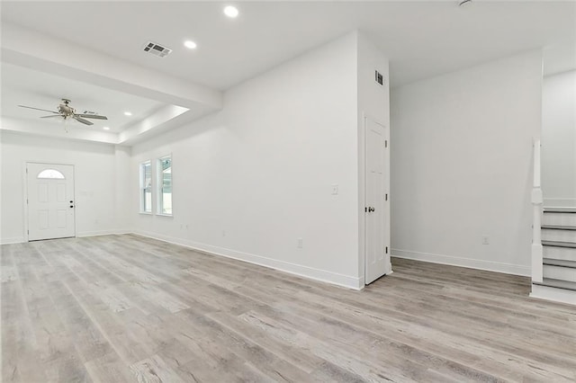 unfurnished living room with a tray ceiling, baseboards, visible vents, and light wood finished floors