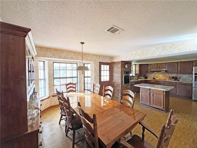 dining space with wallpapered walls, visible vents, and a textured ceiling