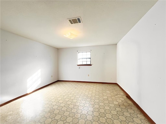 empty room with baseboards, visible vents, light floors, and a textured ceiling