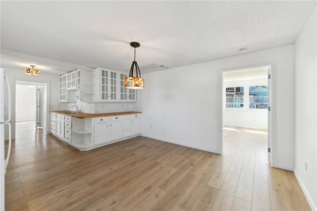 kitchen featuring open shelves, a sink, white cabinets, butcher block counters, and light wood finished floors