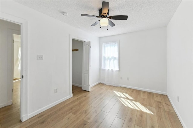 unfurnished bedroom featuring a ceiling fan, light wood-style floors, baseboards, and a textured ceiling