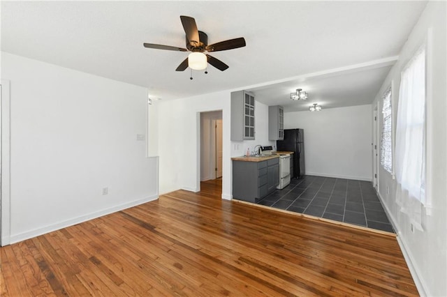 unfurnished living room with dark wood-style floors, baseboards, ceiling fan, and a sink