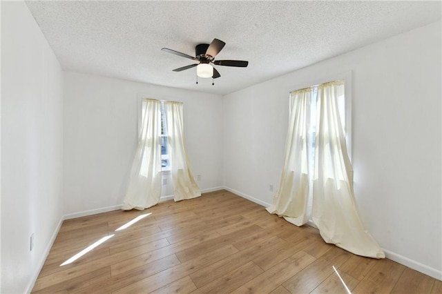 spare room featuring light wood-type flooring, baseboards, a textured ceiling, and ceiling fan