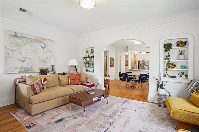 living area with arched walkways, visible vents, built in shelves, and wood finished floors