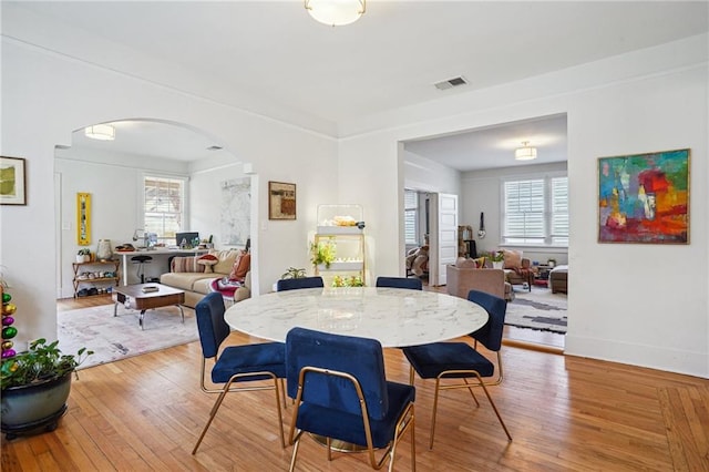 dining space with hardwood / wood-style floors, arched walkways, visible vents, and baseboards