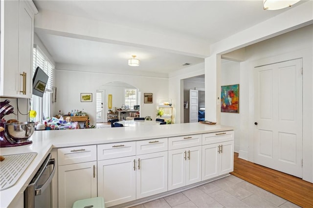 kitchen featuring arched walkways, a peninsula, white cabinetry, and light countertops