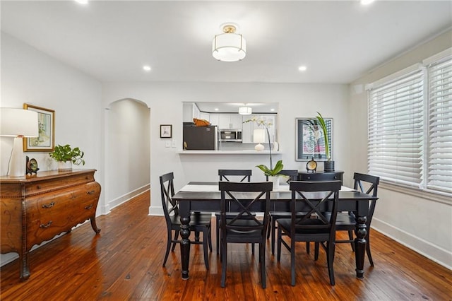 dining area featuring arched walkways, baseboards, and hardwood / wood-style flooring