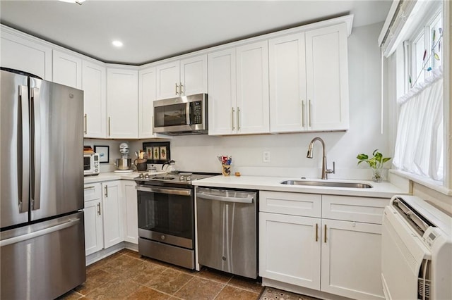 kitchen featuring appliances with stainless steel finishes, white cabinetry, light countertops, and a sink