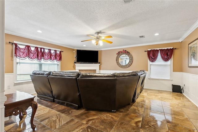 living room with a wainscoted wall, visible vents, a textured ceiling, crown molding, and ceiling fan