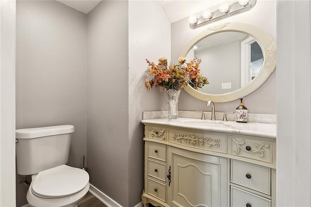 half bathroom with baseboards, toilet, and vanity