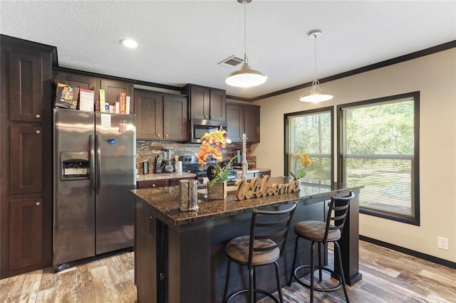 kitchen with light wood finished floors, stainless steel appliances, visible vents, dark brown cabinetry, and decorative backsplash