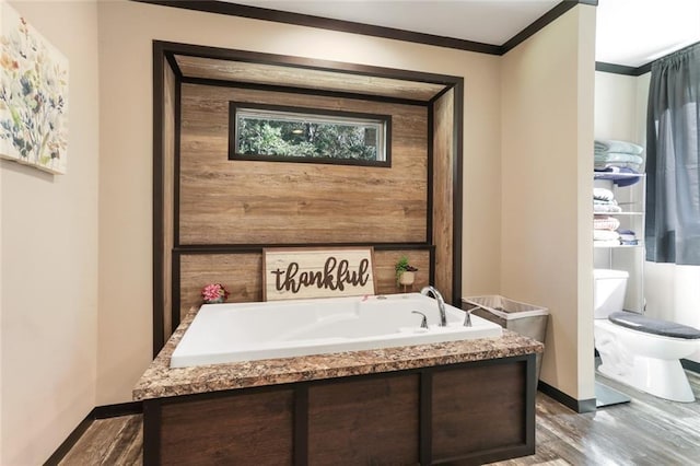 full bathroom with a bath, toilet, baseboards, wood finished floors, and ornamental molding