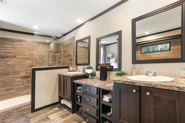 full bathroom featuring wood finished floors, a sink, walk in shower, double vanity, and ornamental molding