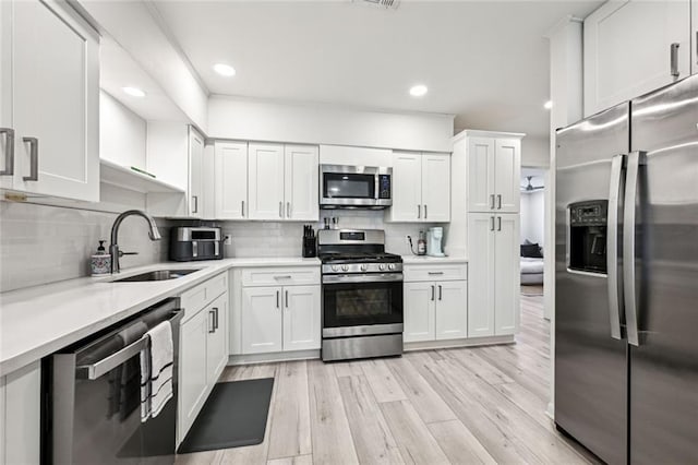 kitchen with a sink, stainless steel appliances, light countertops, white cabinetry, and light wood-type flooring