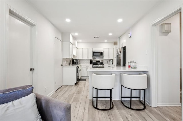 kitchen featuring a breakfast bar, a sink, stainless steel appliances, light wood-style floors, and a peninsula