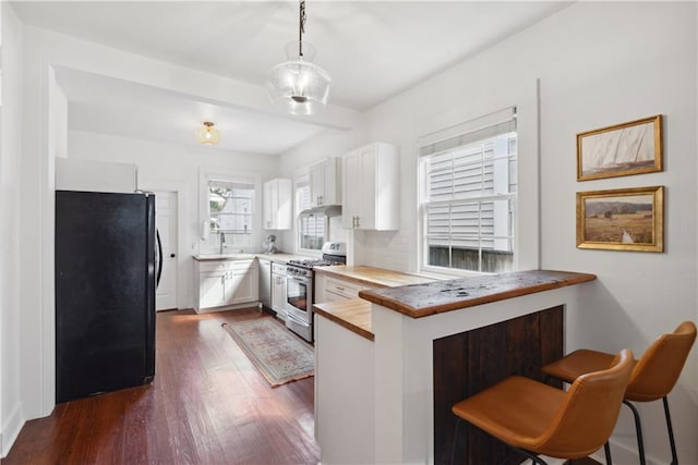 kitchen with freestanding refrigerator, gas stove, a peninsula, white cabinets, and dark wood-style flooring