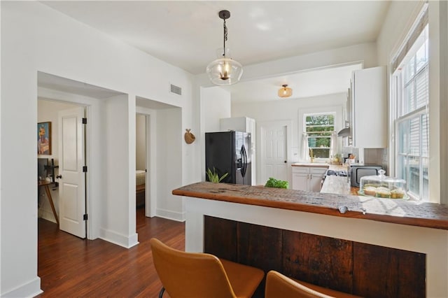 kitchen featuring dark wood-style floors, visible vents, a peninsula, pendant lighting, and black refrigerator with ice dispenser