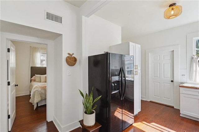 bedroom with dark wood-style floors, black fridge with ice dispenser, baseboards, and visible vents