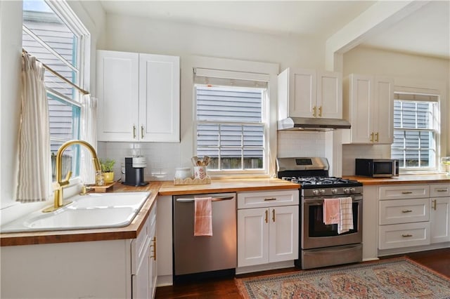 kitchen with under cabinet range hood, a sink, white cabinetry, stainless steel appliances, and butcher block counters