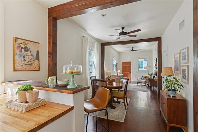 dining area featuring ceiling fan, visible vents, beamed ceiling, and dark wood-style floors