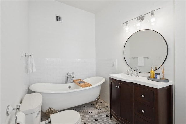 full bathroom featuring vanity, visible vents, a soaking tub, tile walls, and toilet