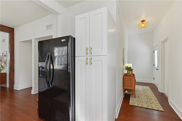 interior space featuring visible vents, baseboards, black fridge, white cabinets, and dark wood-style flooring