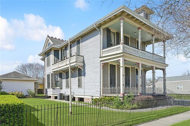 view of front facade featuring fence, a front yard, covered porch, cooling unit, and a balcony