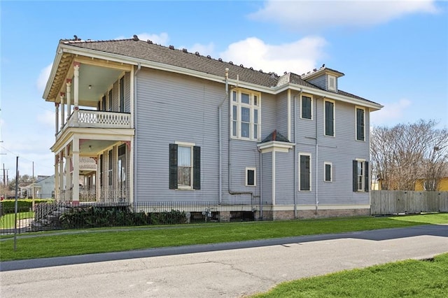 view of side of home with a balcony, a yard, and fence