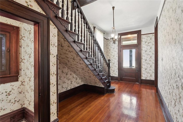 entryway featuring wood-type flooring, wallpapered walls, baseboards, a chandelier, and stairs