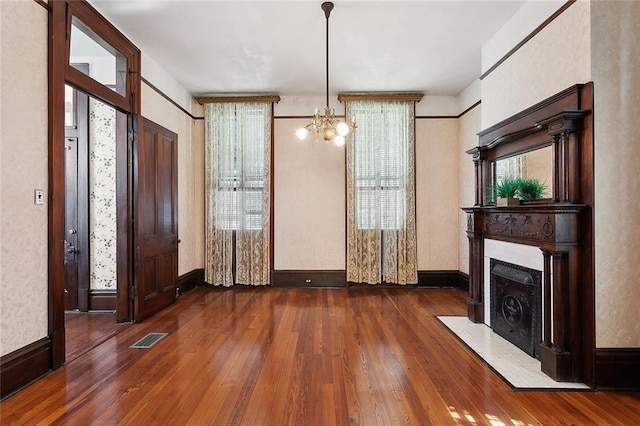 interior space with visible vents, a fireplace with flush hearth, hardwood / wood-style floors, baseboards, and a chandelier