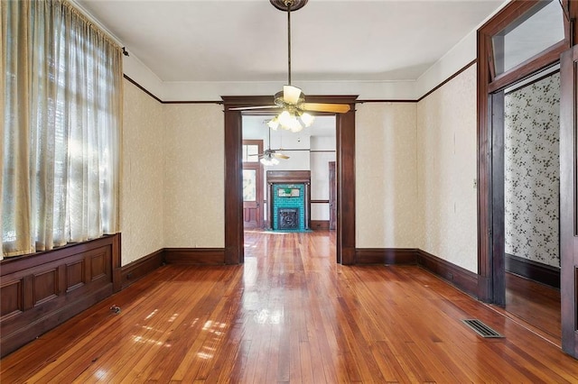 unfurnished dining area featuring visible vents, baseboards, a fireplace with flush hearth, hardwood / wood-style floors, and a ceiling fan