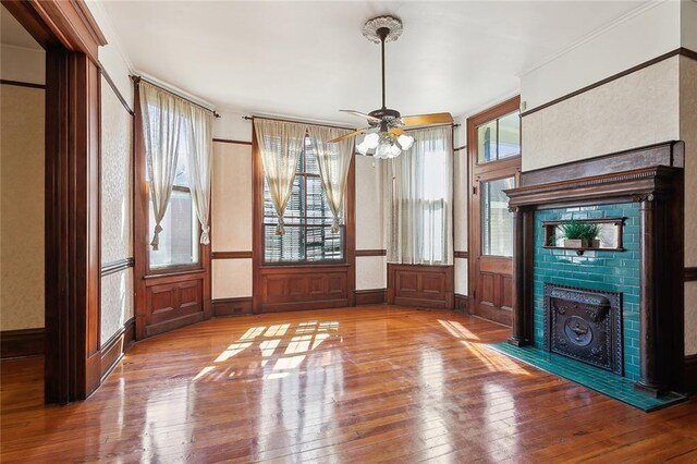 unfurnished living room featuring a fireplace with flush hearth, a healthy amount of sunlight, crown molding, and wood-type flooring