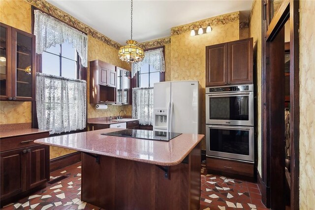 kitchen with a kitchen island, white refrigerator with ice dispenser, double oven, wallpapered walls, and black electric cooktop