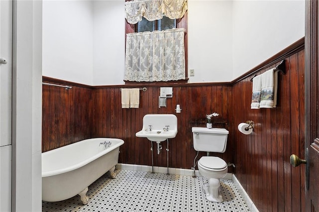 full bath with a freestanding tub, a wainscoted wall, toilet, and wooden walls