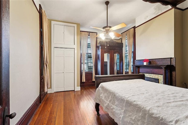 bedroom with ceiling fan, a fireplace, baseboards, and hardwood / wood-style floors