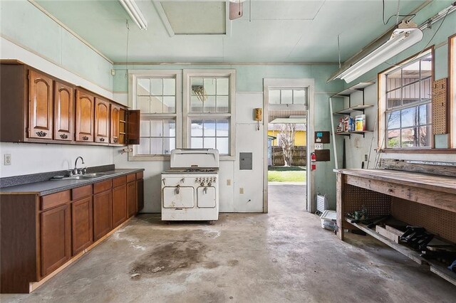 kitchen featuring brown cabinets, a sink, gas range gas stove, dark countertops, and unfinished concrete floors