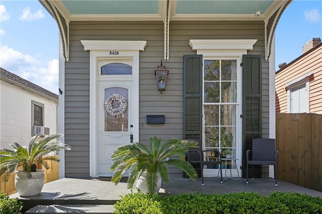 doorway to property with covered porch and fence