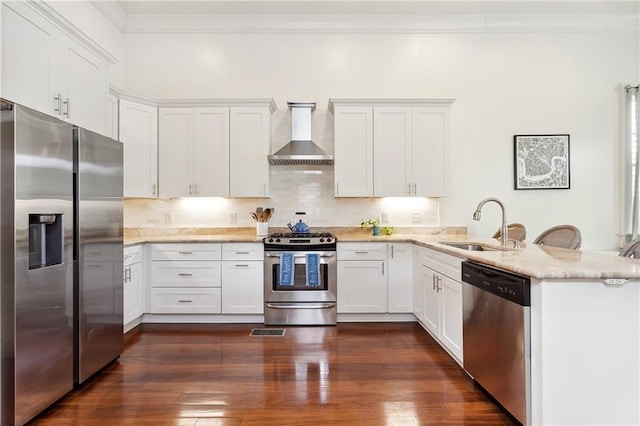 kitchen featuring dark wood-style floors, a peninsula, a sink, appliances with stainless steel finishes, and wall chimney exhaust hood